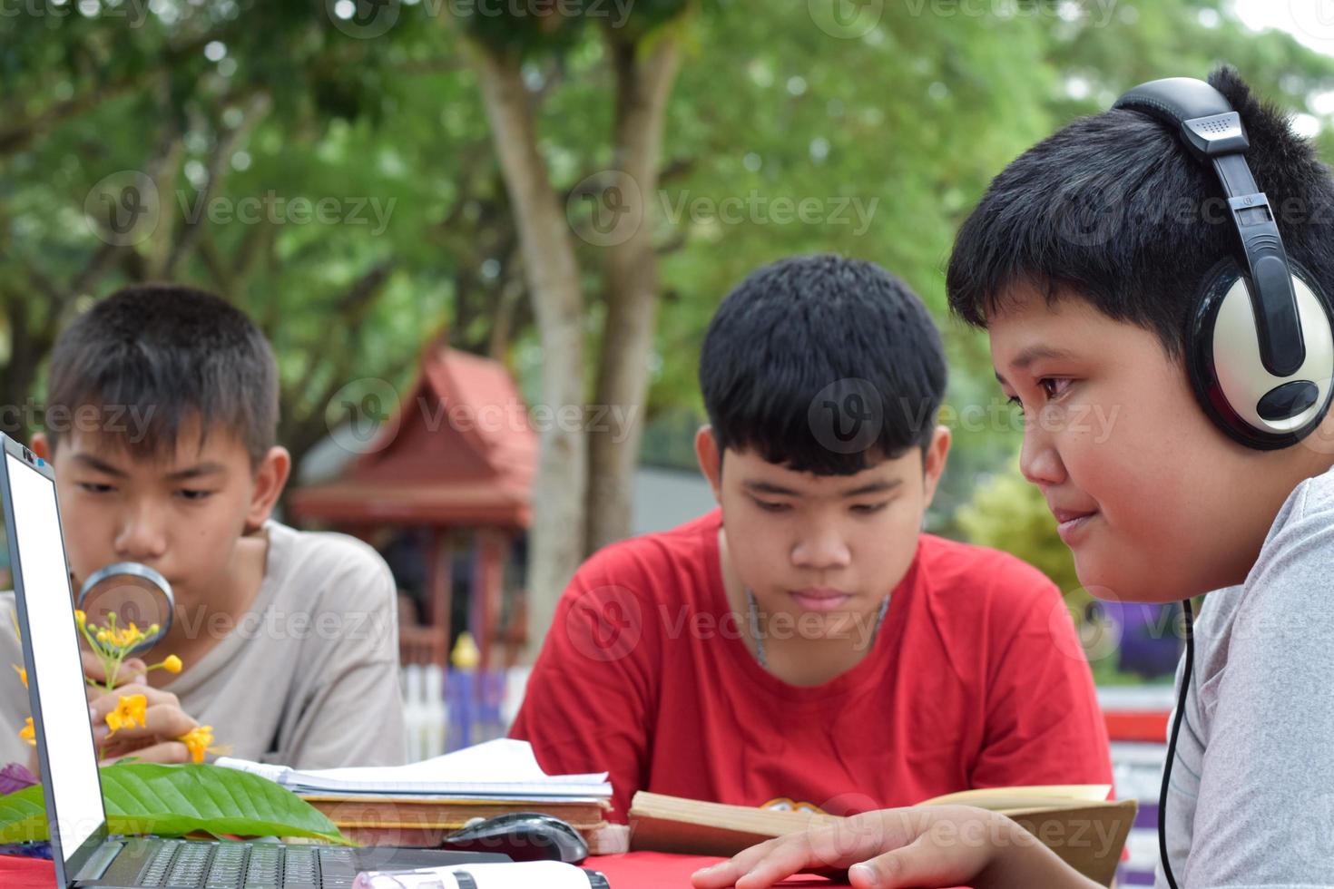 Young Asian boys doing homework and do the reports about various species of tropical forests by using laptops, magnifiers, notebooks, pocket binoculars and tablets, mockup laptop concept. photo