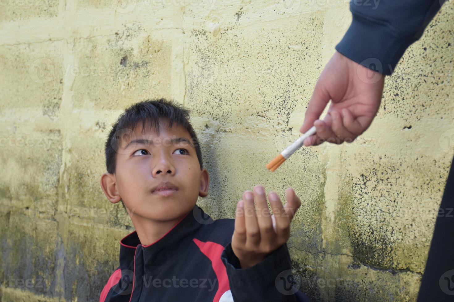 Boy learning to smoke by himself in the area behind the school fence which is a hidden place for people, bad influence of secondary school or junior high school life, addiction. photo