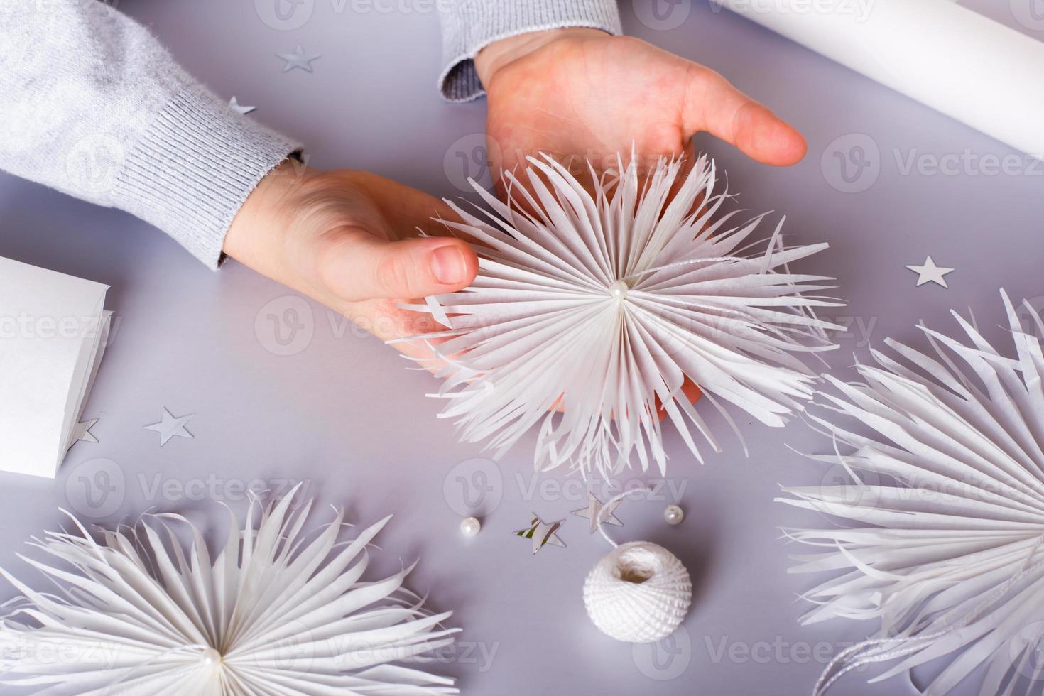 Children's hands hold a paper snowflake with a thread and a bead. Handmade decor photo