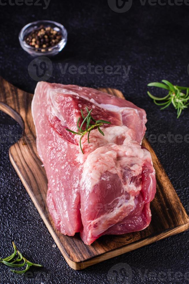 Large piece of pork, rosemary and salt on a cutting board on a black background. Vertical view photo
