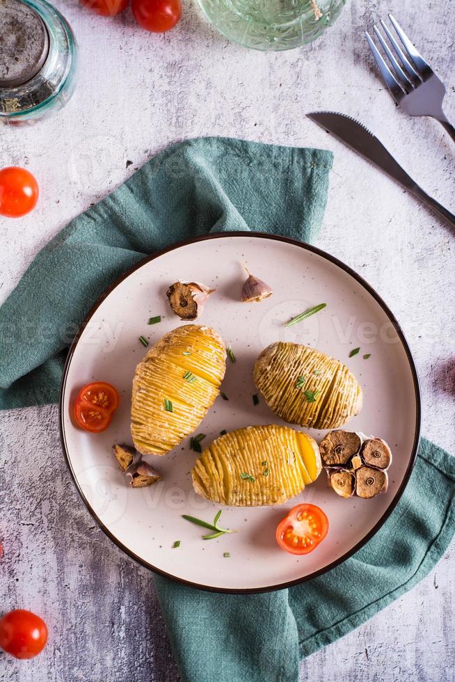 Baked hasselback potatoes with garlic and rosemary on a plate. Homemade lunch. Top and vertical view photo