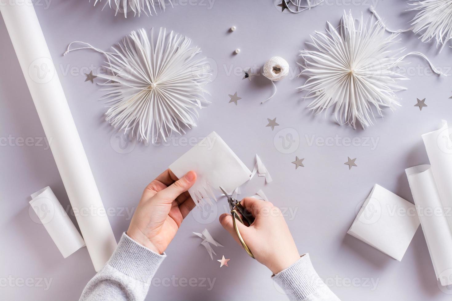 Children's hands with scissors cut out a Christmas snowflake from paper. Handmade decor photo