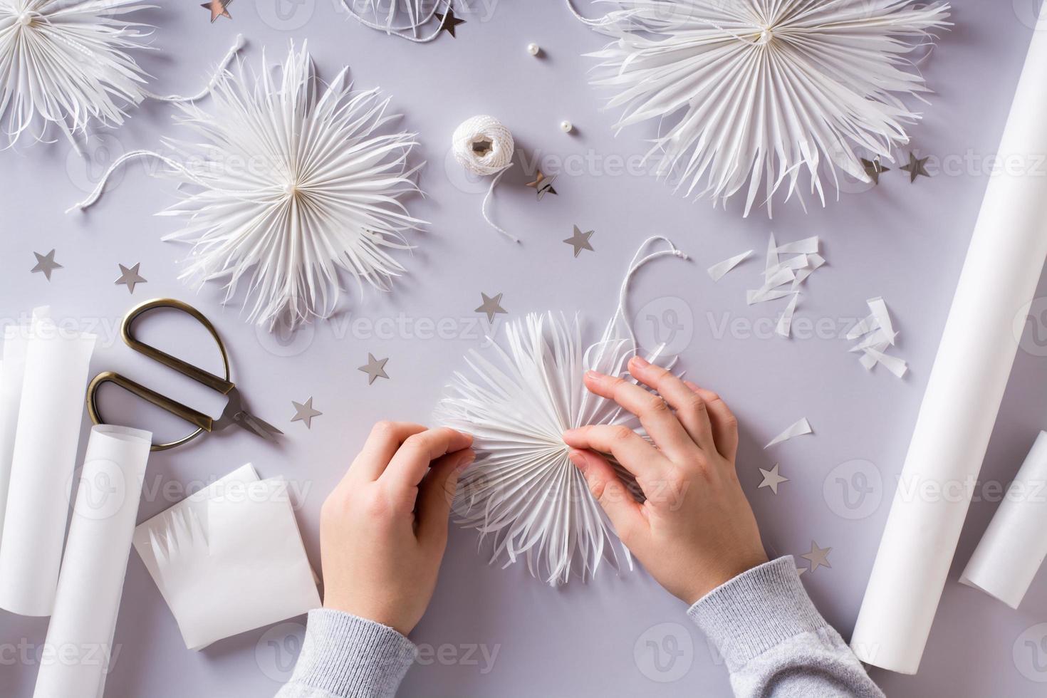 Children's hands glue a bead to a paper snowflake on a gray background. Handmade decor. Top view. photo