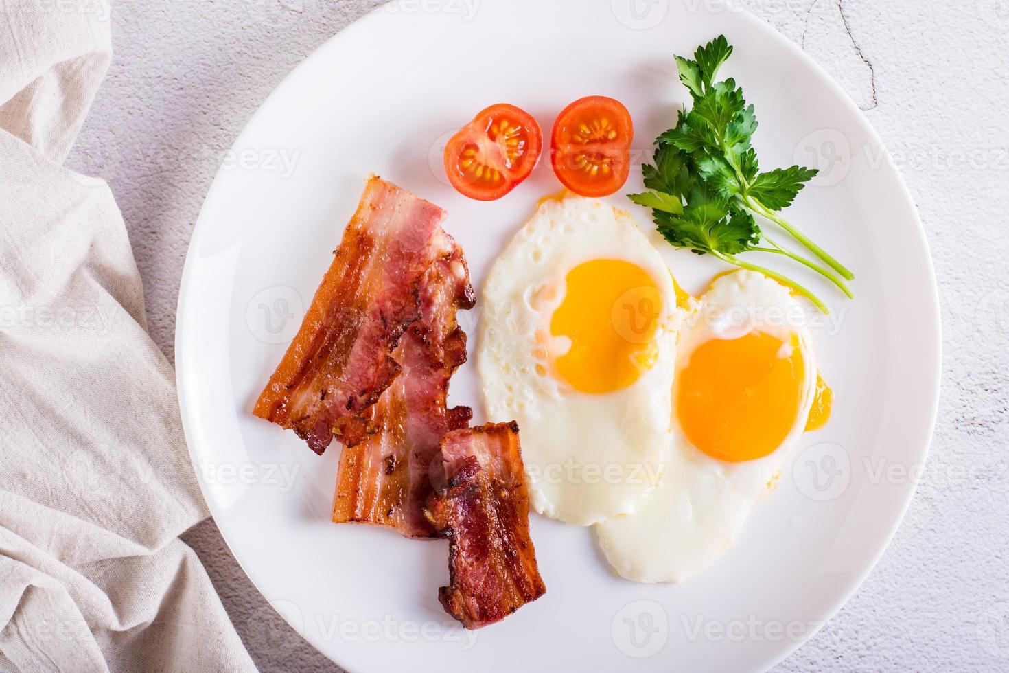 Fried eggs and bacon, tomatoes and parsley on a plate. Homemade breakfast. Top view. Closeup photo