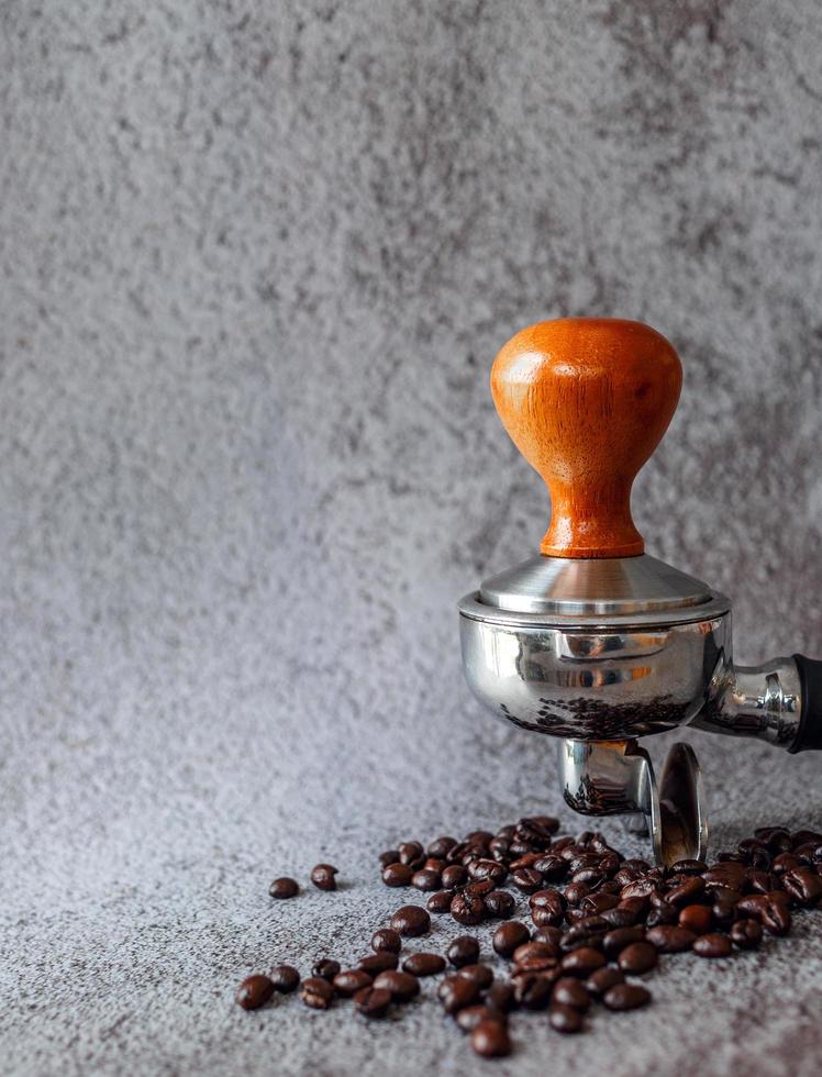 Equipment in a coffee shop of barista coffee tool portafilter with tamper and dark roasted coffee beans on gray background photo