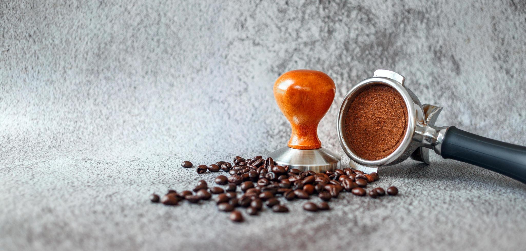 Equipment in a coffee shop of barista coffee tool portafilter with tamper and dark roasted coffee beans on gray background photo