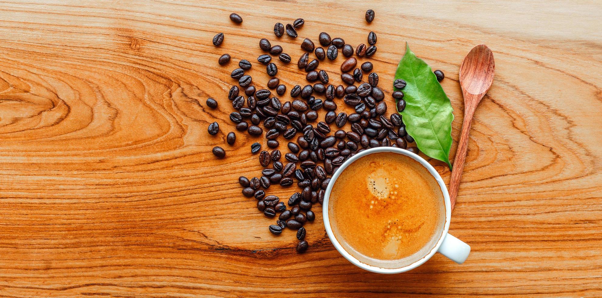 Top view of Espresso coffee cup and dark roasted coffee beans with green coffee leaf  on wooden background photo