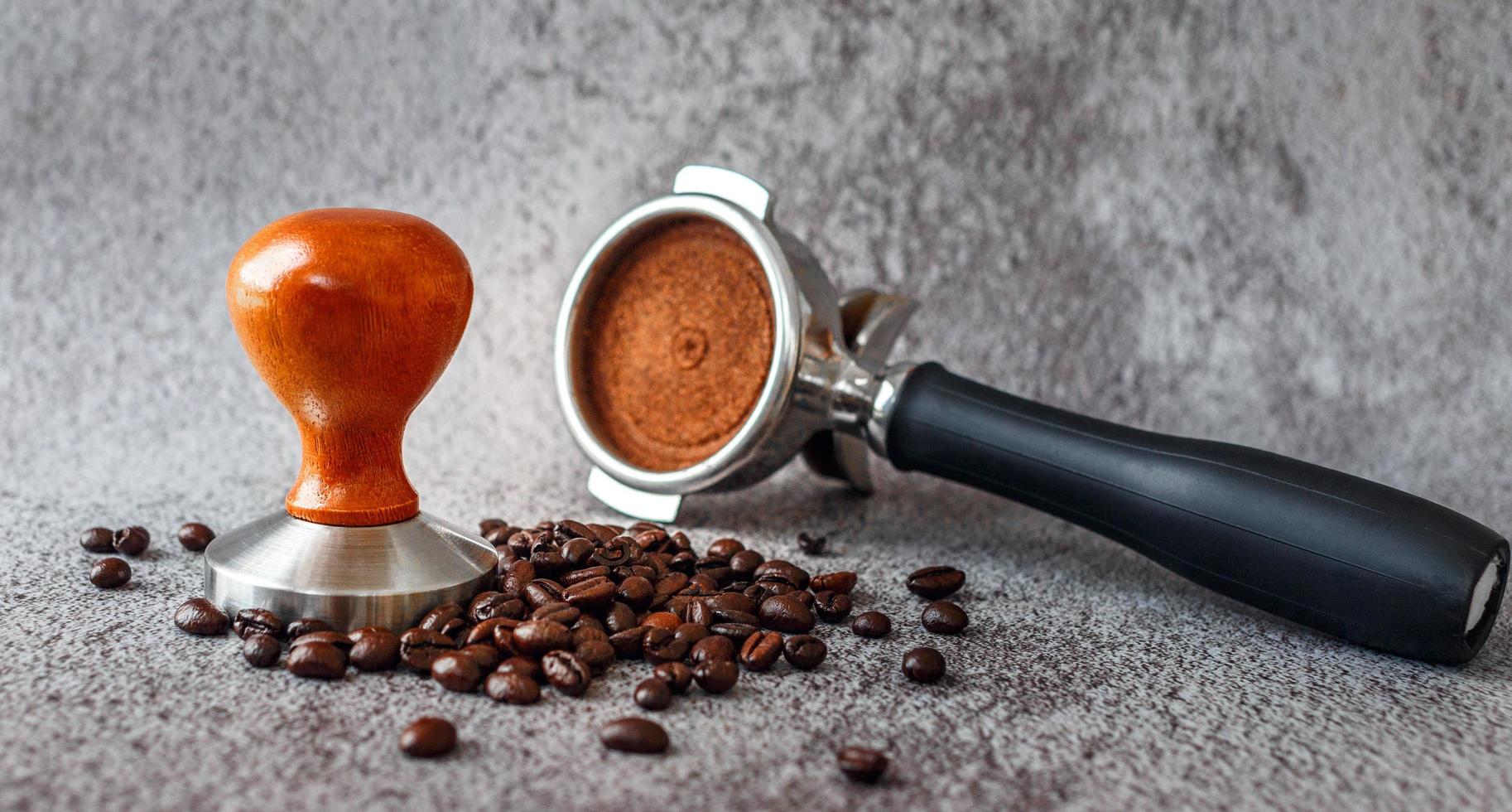 Equipment in a coffee shop of barista coffee tool portafilter with tamper and dark roasted coffee beans on gray background photo