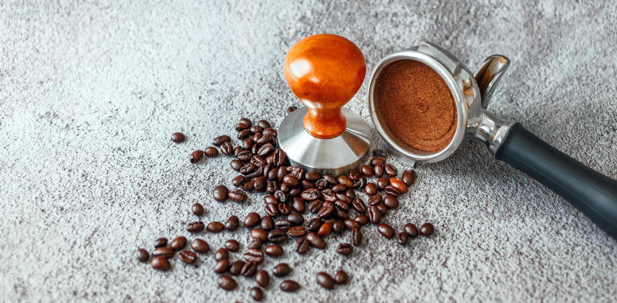 Equipment in a coffee shop of barista coffee tool portafilter with tamper and dark roasted coffee beans on gray background photo