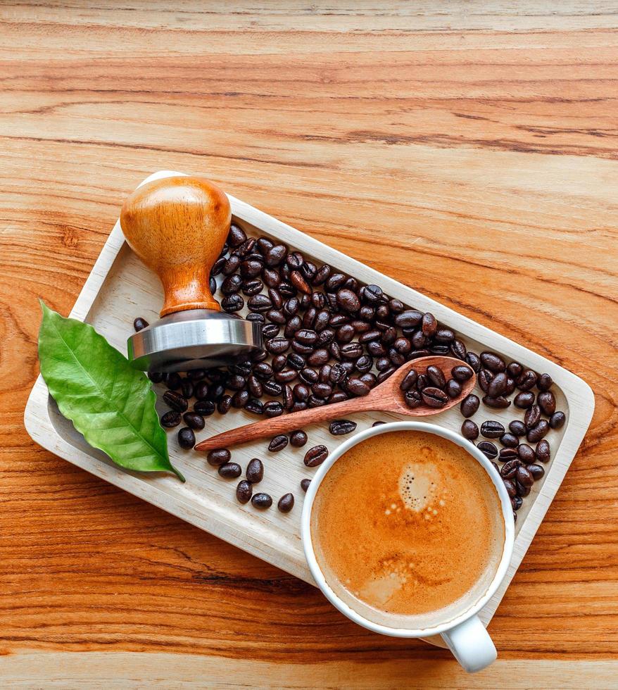 Top view of Espresso coffee cup and equipment of barista coffee tool tamper and dark roasted coffee beans with green coffee leaf  on wooden table photo