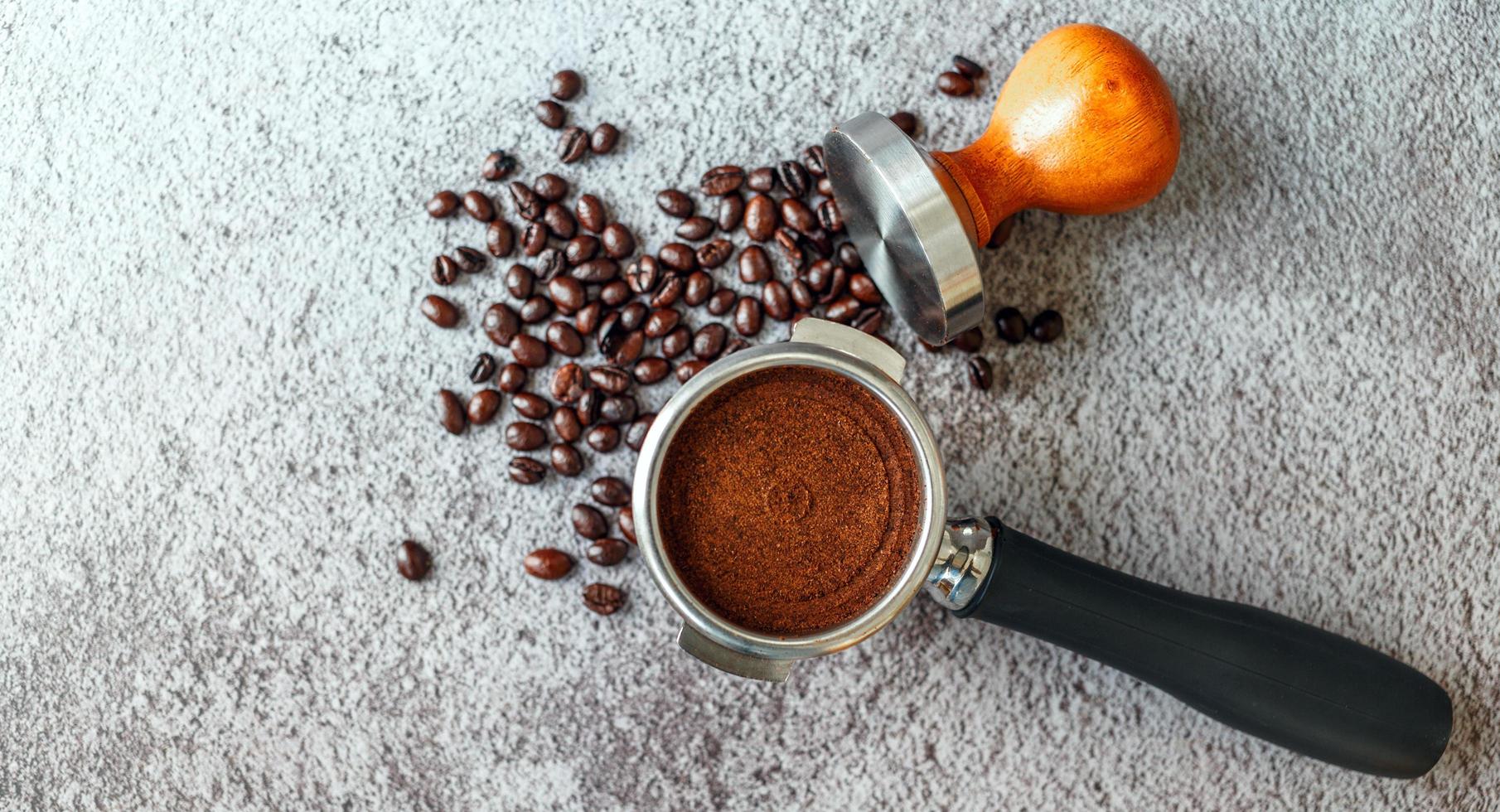 Equipment in a coffee shop of barista coffee tool portafilter with tamper and dark roasted coffee beans on gray background photo