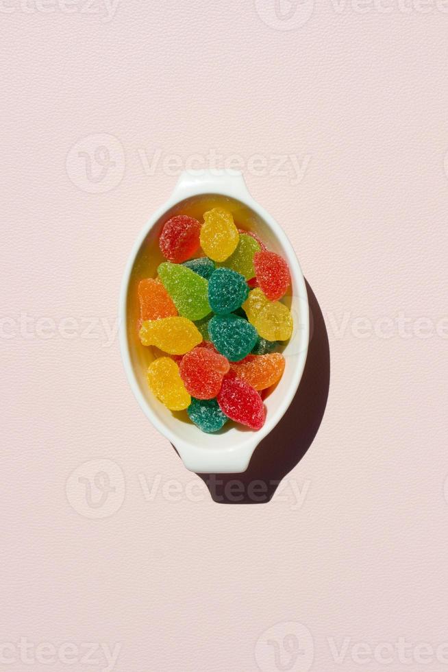 Colorful sweet jelly in white bowl on pink background with free place for text,harmful snack for kids,plate full of candies,vertical image for banner,advertising,design with copyspace,flat lay photo