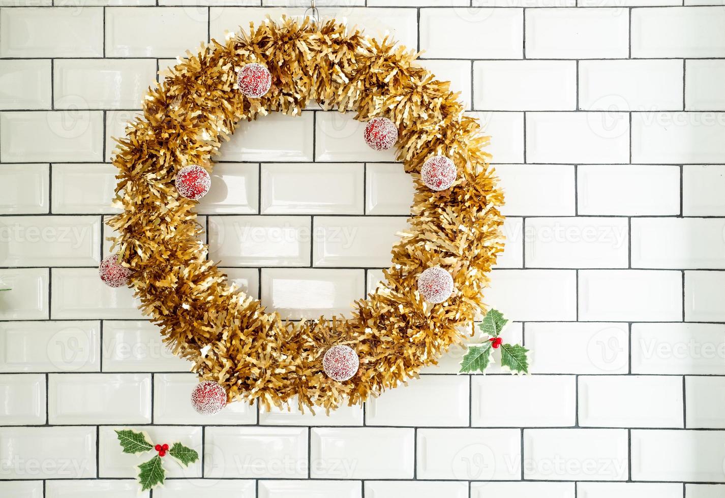 A traditional Christmas decoration for the new year. A wreath of gold coniferous wood with red christmas ball on whit wall background photo
