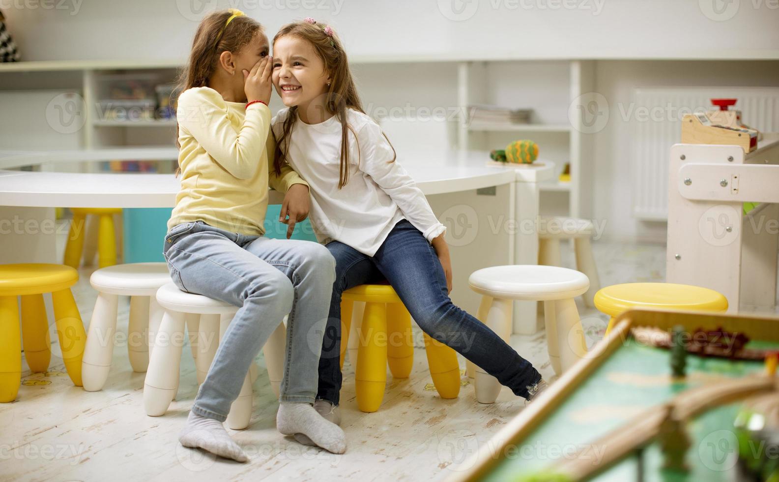 Little girl whispering something in an ear of her friend photo