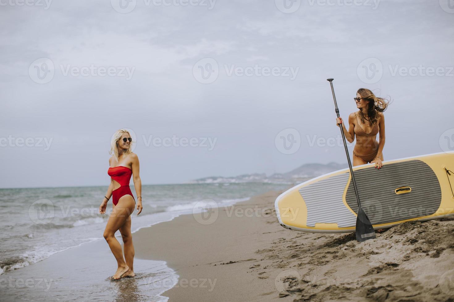Two young women with paddle board on the beach on a summer day photo