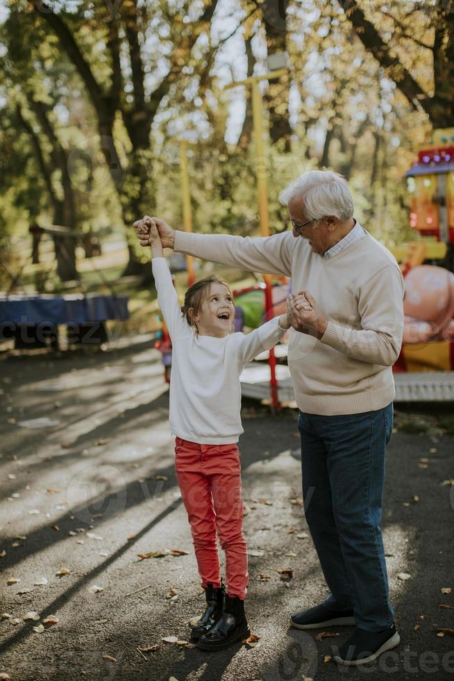 Grandfather having fun with his little granddaughter in the amusement park photo