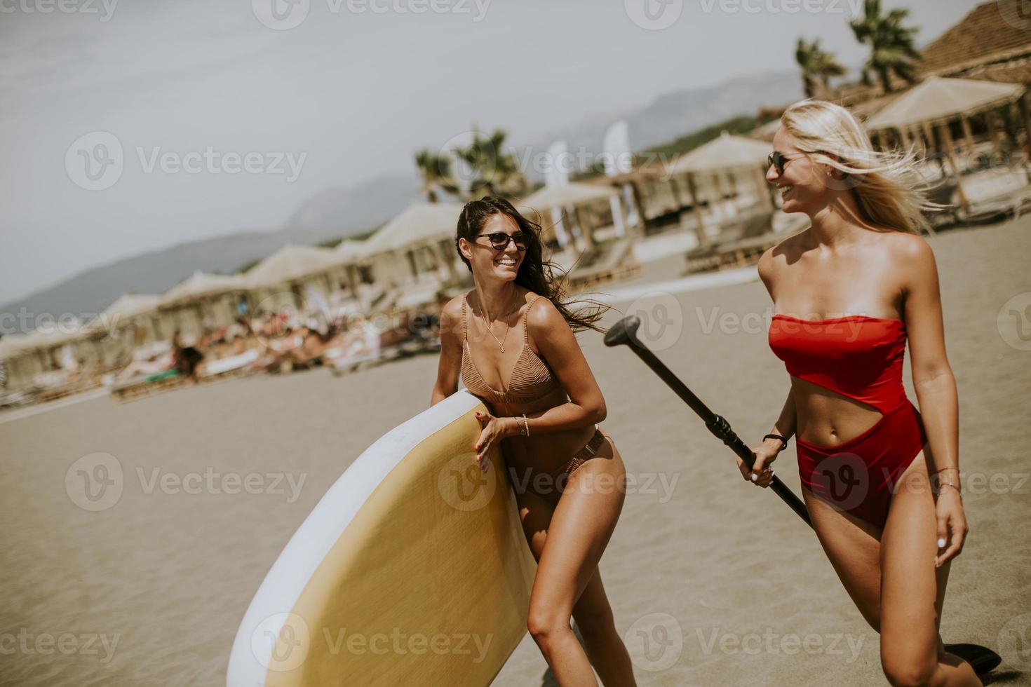 Two young women with paddle board on the beach on a summer day photo