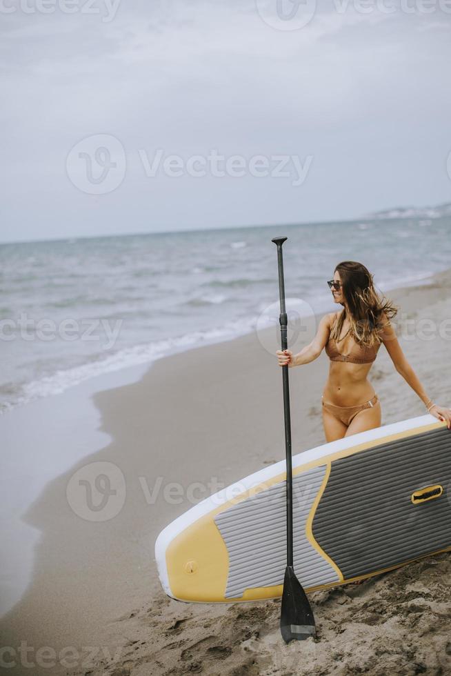 Young woman with paddle board on the beach on a summer day photo