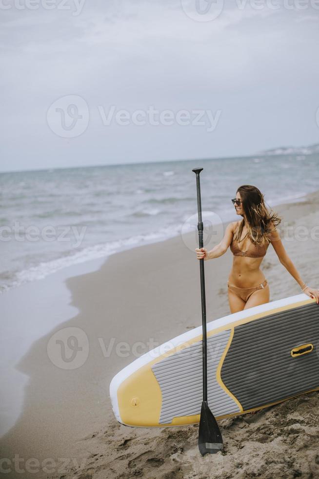 mujer joven con paddle board en la playa en un día de verano foto