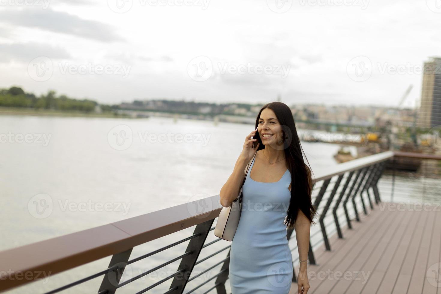 mujer joven usando un teléfono móvil mientras camina por el paseo del río foto