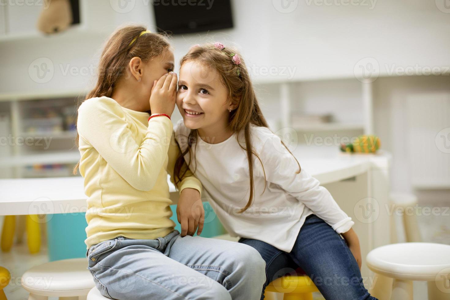 Little girl whispering something in an ear of her friend photo