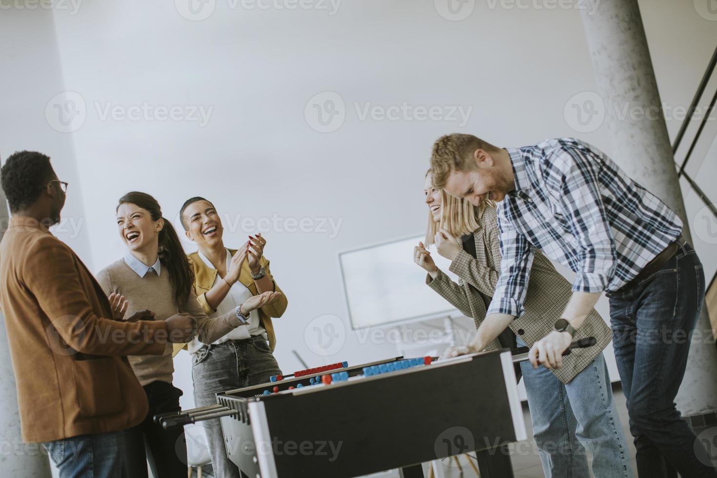 jóvenes empresarios multiétnicos casuales jugando futbolín y relajándose en la oficina foto