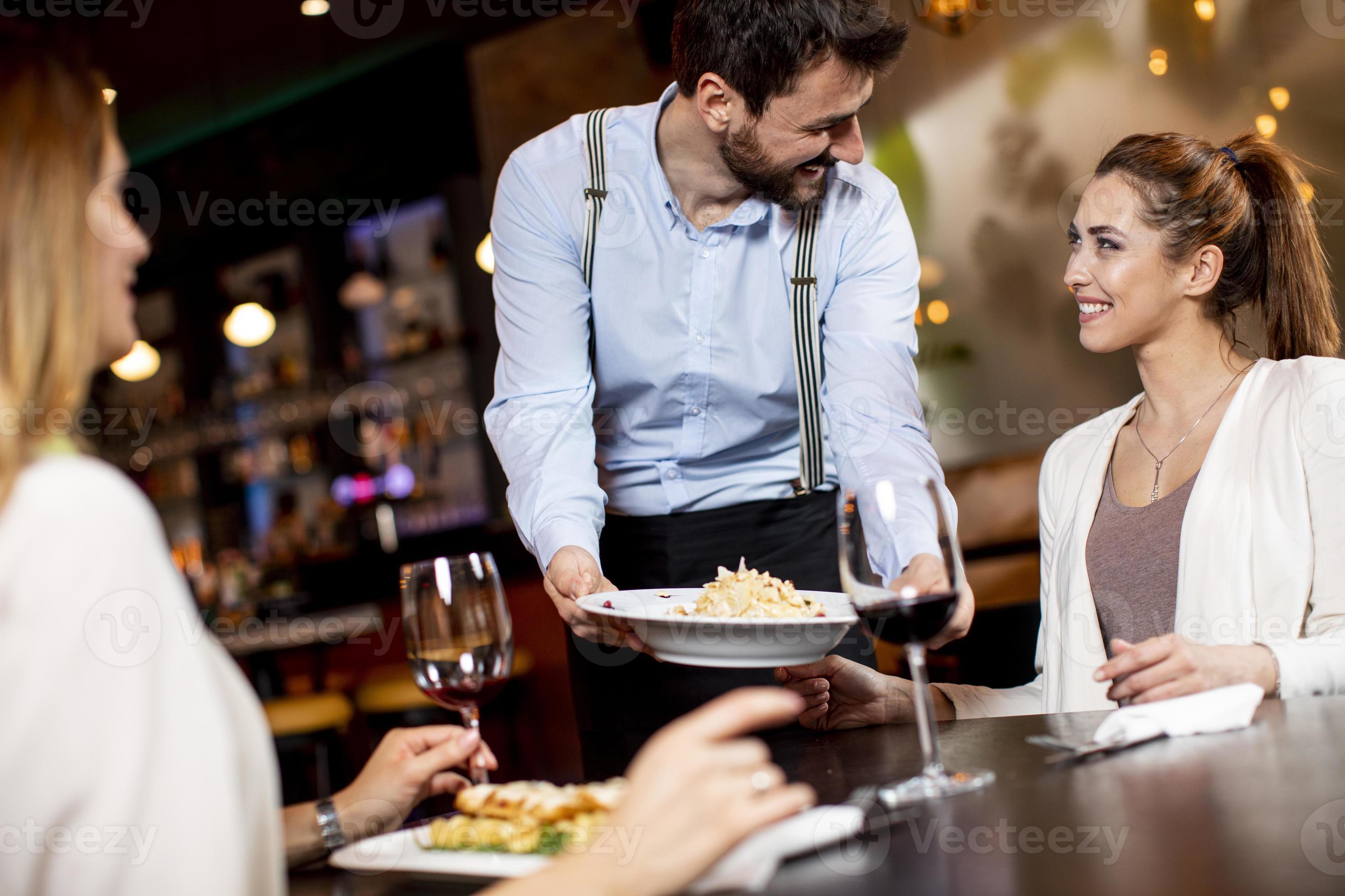 Young waiter serving food to female customers in the restaurant
