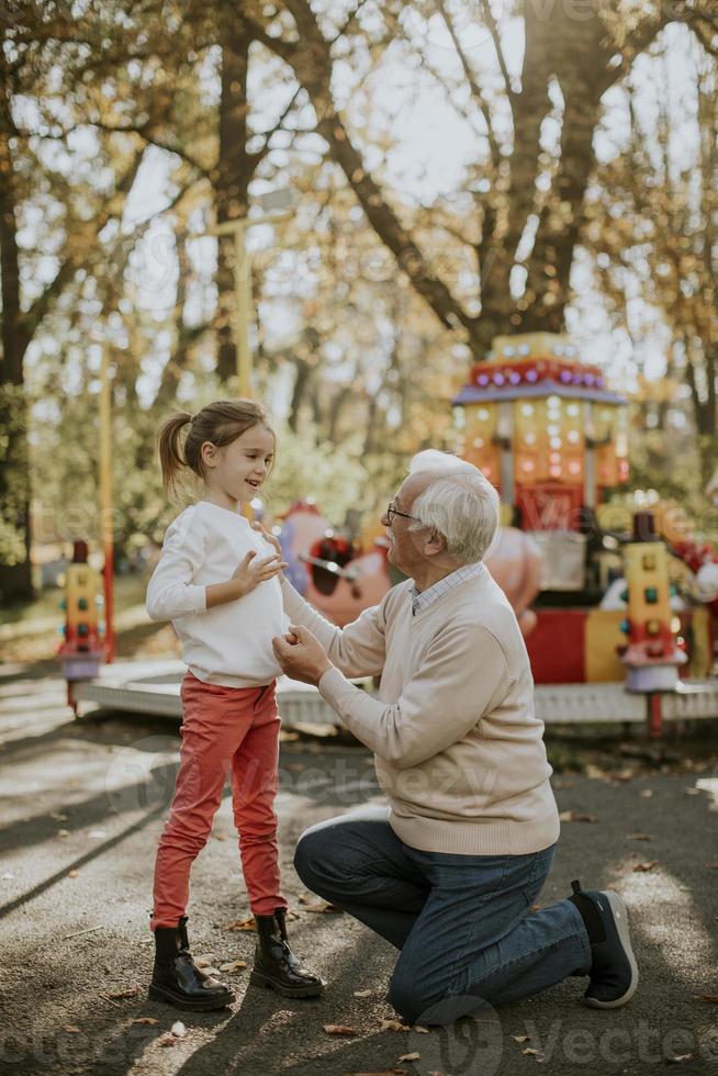 Grandfather having fun with his little granddaughter in the amusement park photo