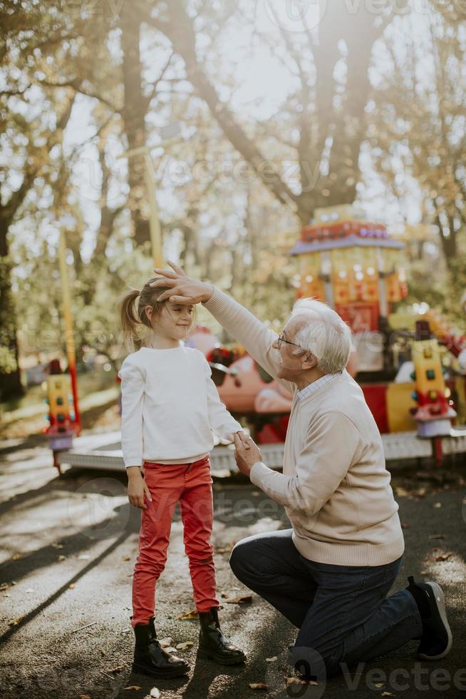 Grandfather having fun with his little granddaughter in the amusement park photo