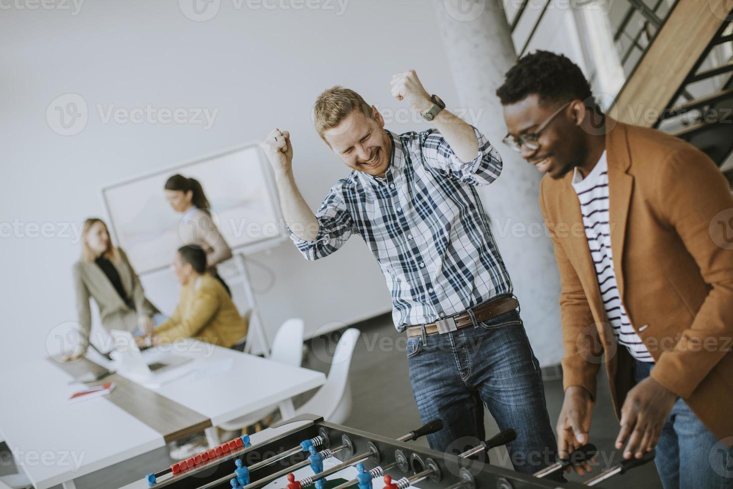 jóvenes empresarios multiétnicos casuales jugando futbolín y relajándose en la oficina foto