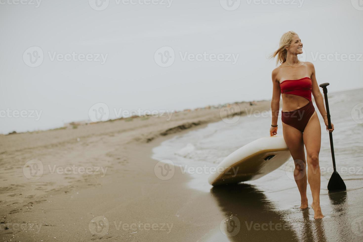 mujer joven caminando con paddle board en la playa en un día de verano foto