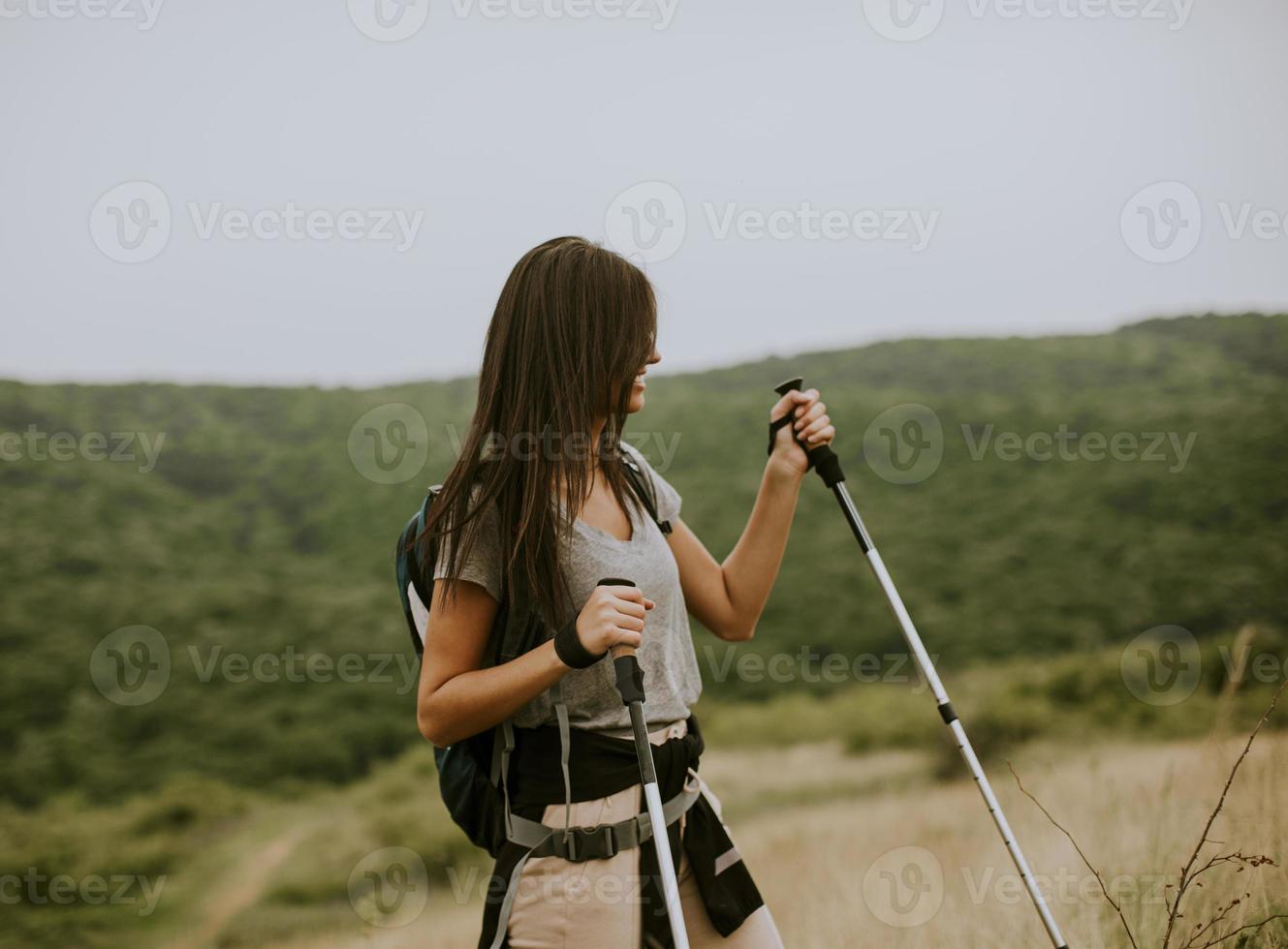 mujer joven sonriente caminando con mochila en las verdes colinas foto