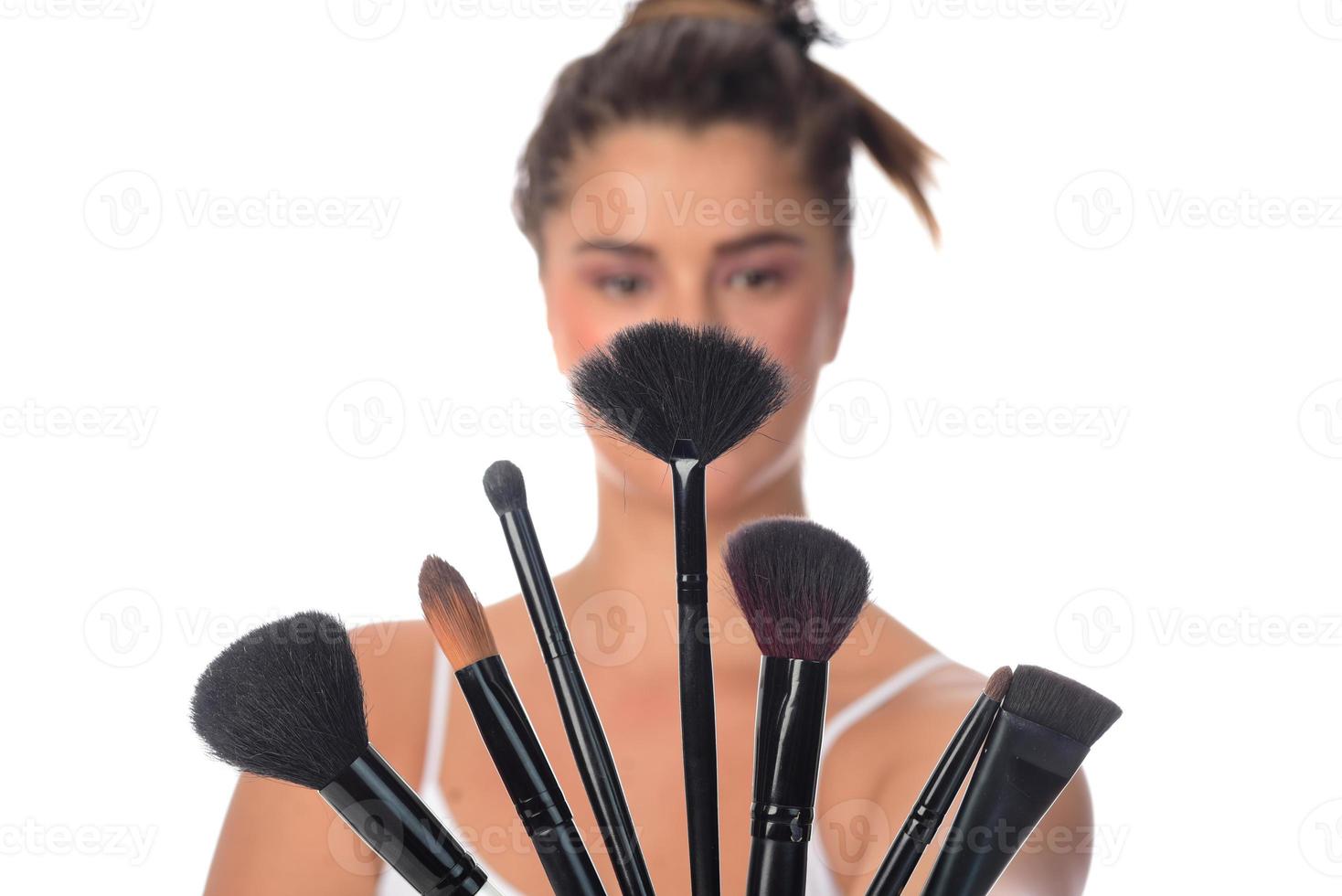 jovencita posando con pinceles de maquillaje en un fondo blanco foto