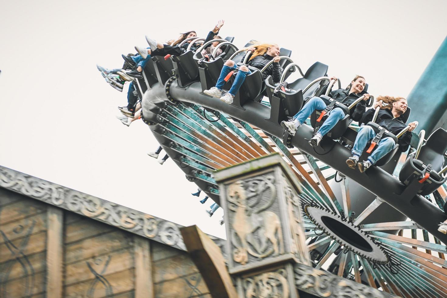 people having fun in amusement park. Young friends on thrilling roller coaster ride photo