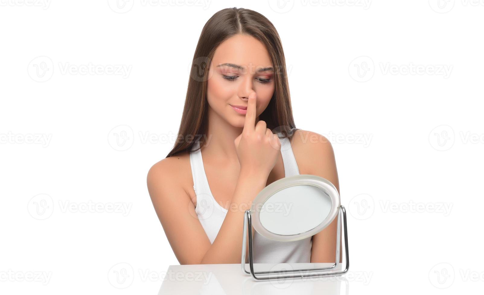 Acne prone skin concept. Young woman looking at mirror at home, checking her face skin photo