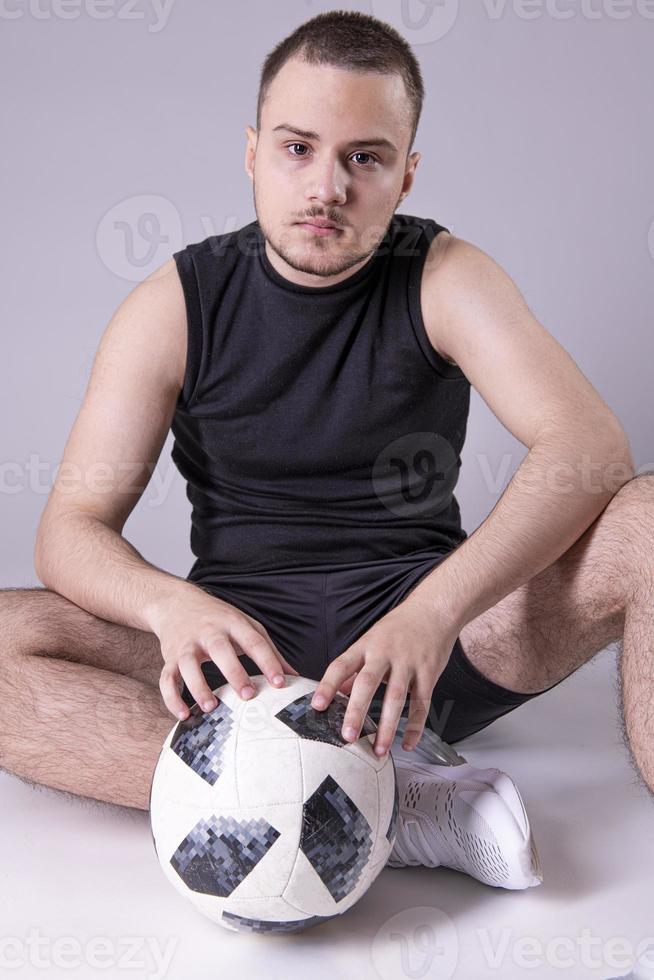 joven feliz 20s ventilador apoyo fútbol deporte equipo sostener en mano balón de fútbol. aislado sobre fondo gris sólido liso foto