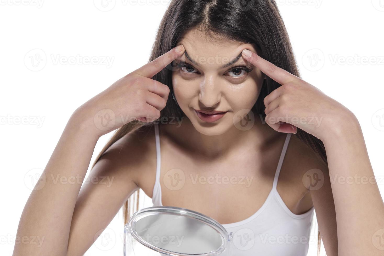 retrato de una niña poniendo ungüento cosmético en la cara mientras mira el espejo interior foto