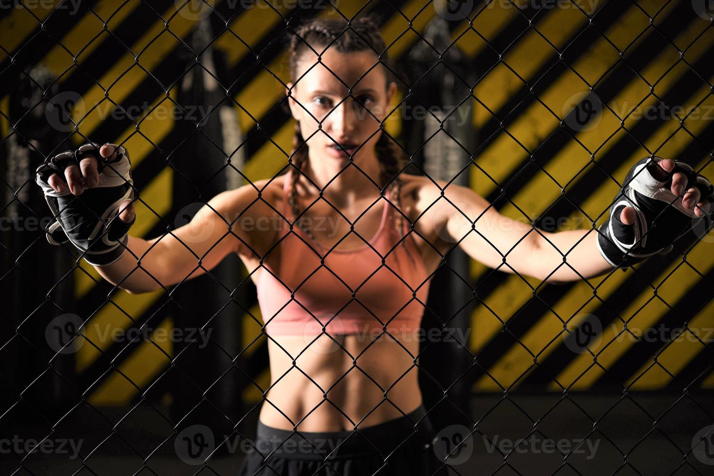 A female trainee of mixed martial arts wearing a hand wrap warms up within the ring cage by stretching her back and legs. photo