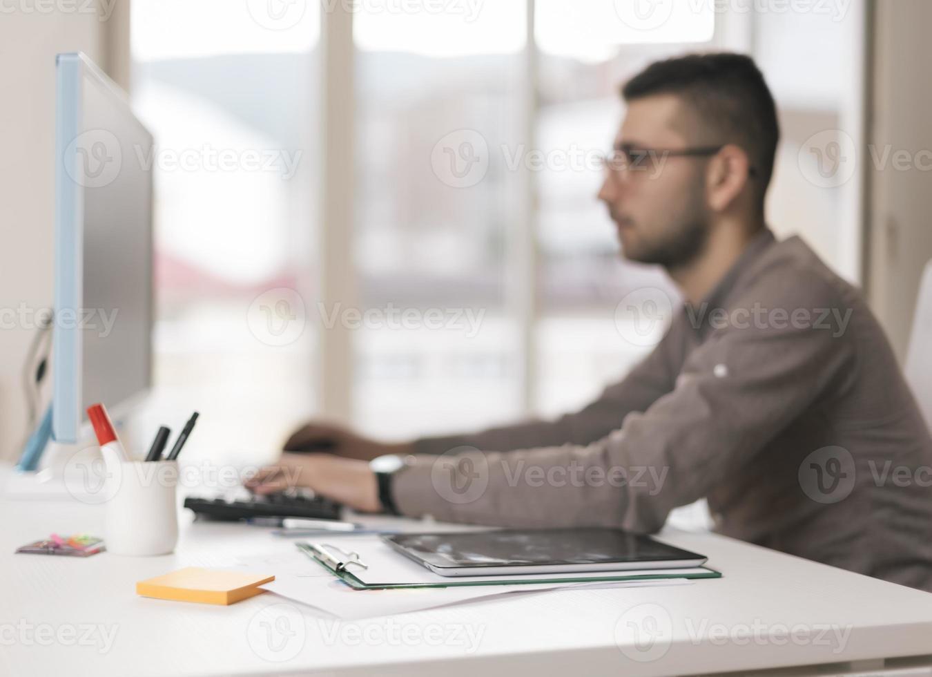 Portrait of young man sitting at his desk in the office working on is laptop photo