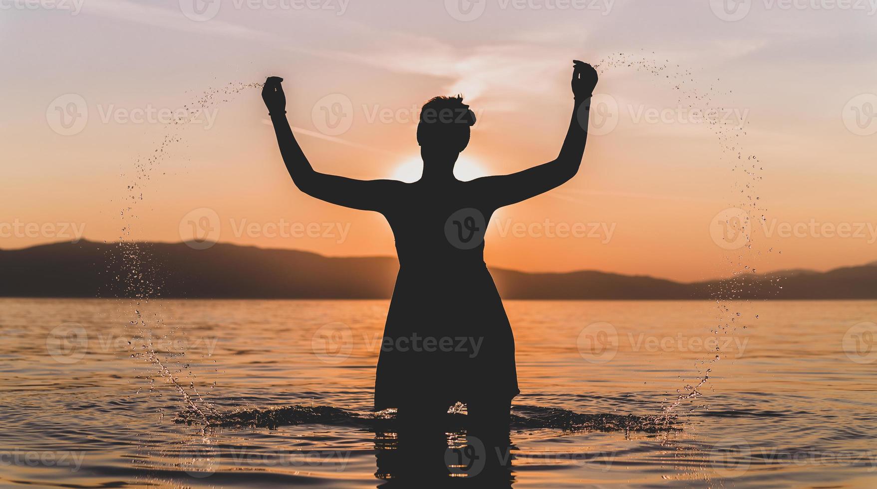 silhouettes of beautiful female model at sunset, sunrise on the background of the sea, the sun, the clouds in fiery red, orange colors photo