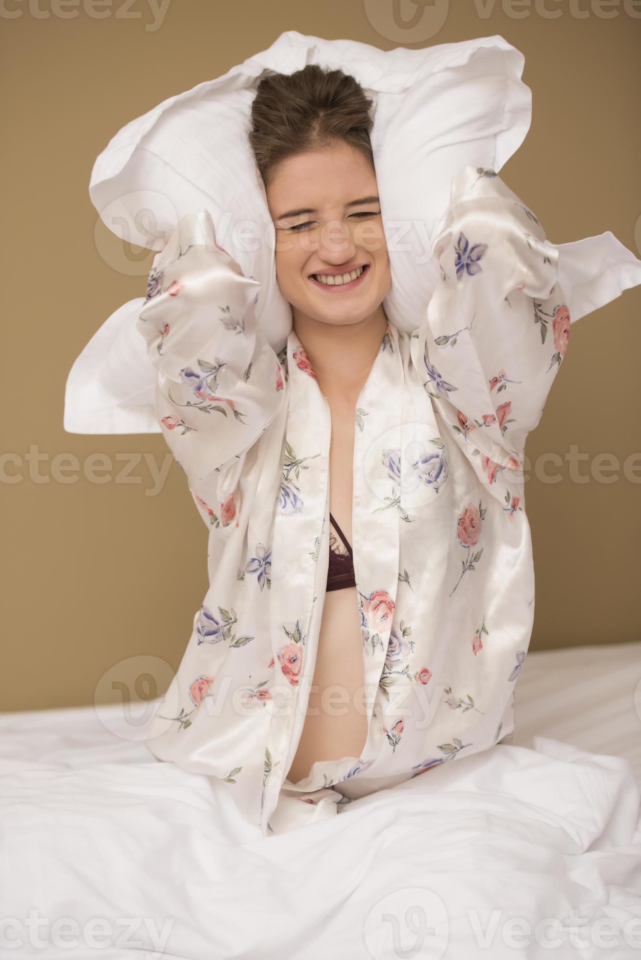 Young woman hugging pillow on comfortable bed with silky linens
