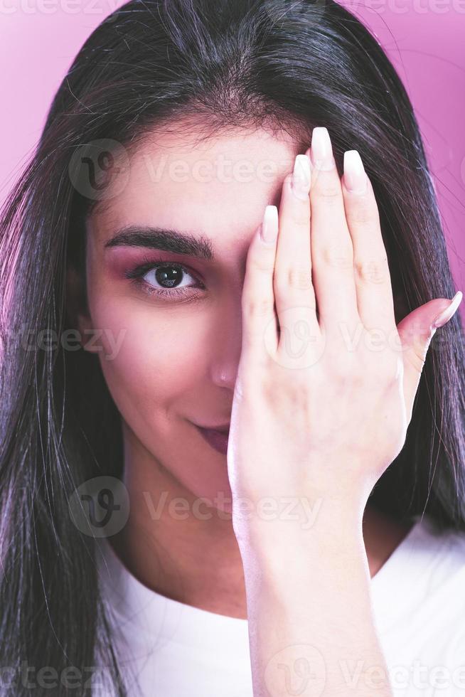 foto de una mujer joven y atractiva que cubre el brazo del ojo chequeo oftalmología de la visión aislada sobre fondo de color rosa