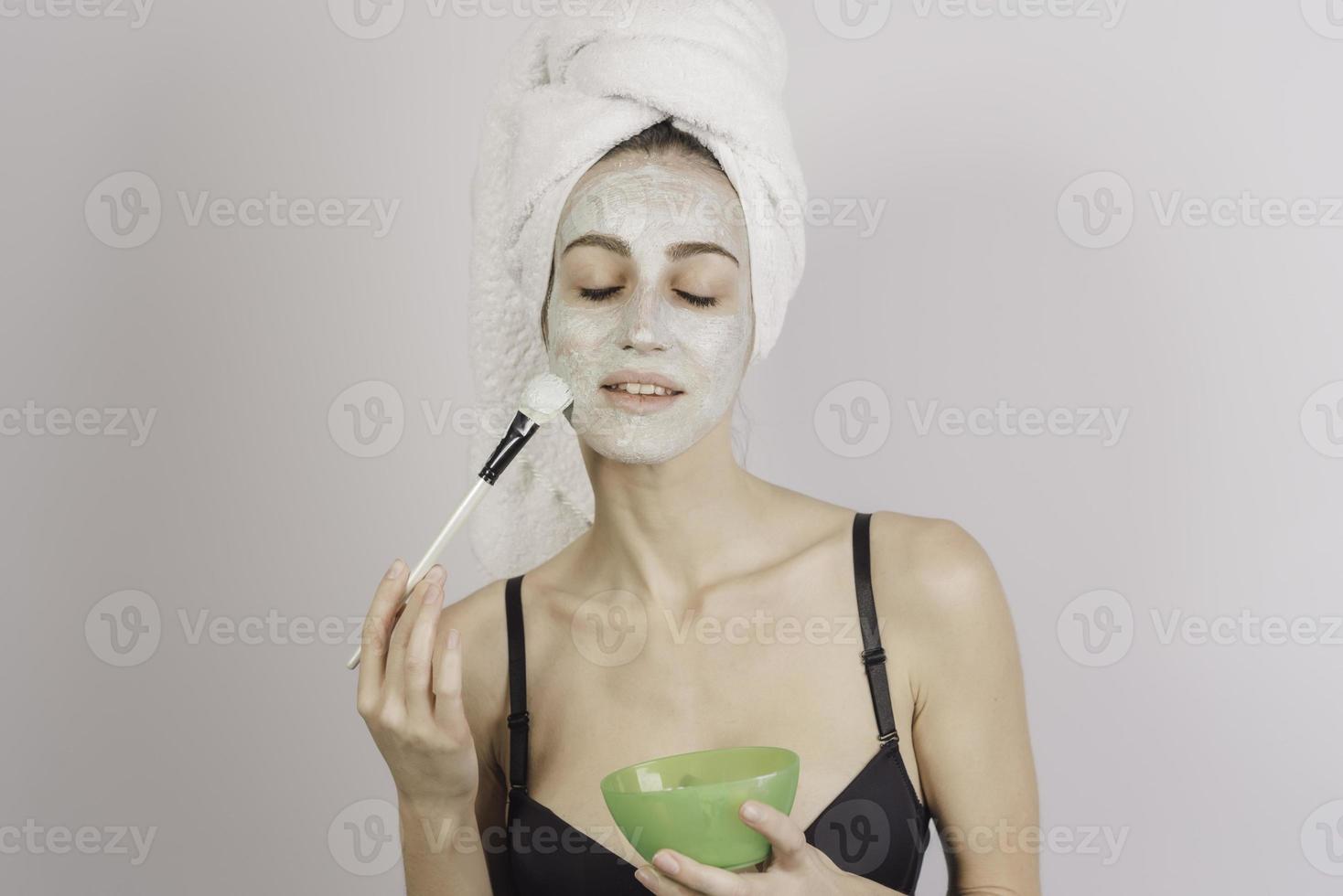 Spa Woman applying Facial clay Mask. Beauty Treatments. Close-up portrait of beautiful girl with a towel on her head applying facial mask. photo