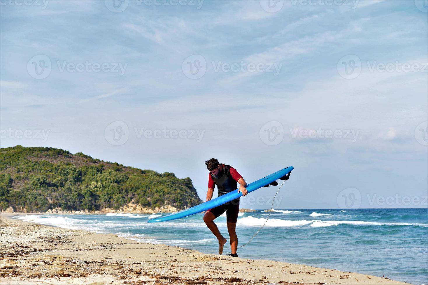 A man is standing with a surf in his hands on the sea shore. photo