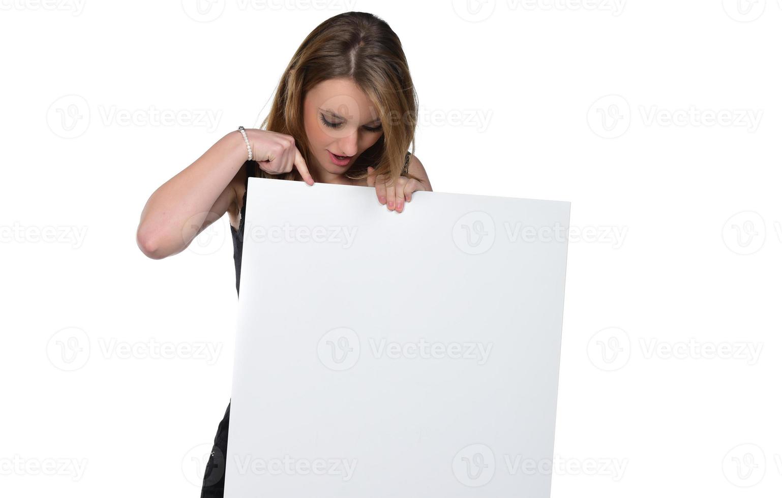 retrato de una mujer joven y hermosa mirando a la cámara con un cartel blanco en blanco que se muestra con el dedo.aislado en blanco foto