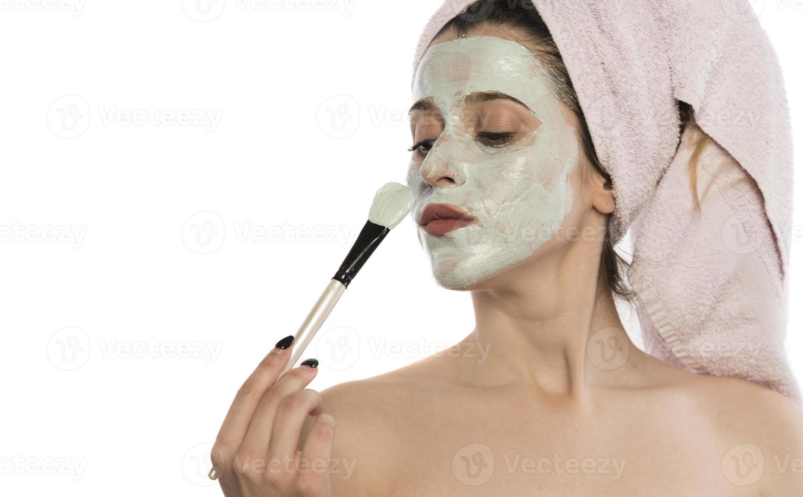 Beautiful woman having clay facial mask apply by beautician. photo