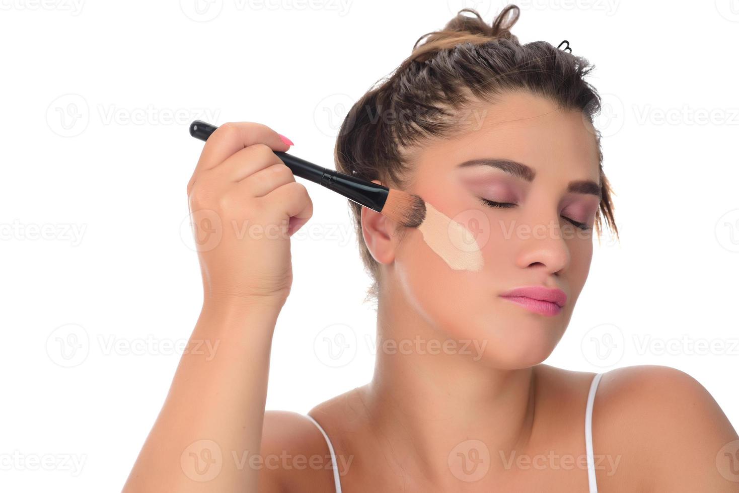 Portrait of a young woman applying make up on her face. Isolated on white background photo