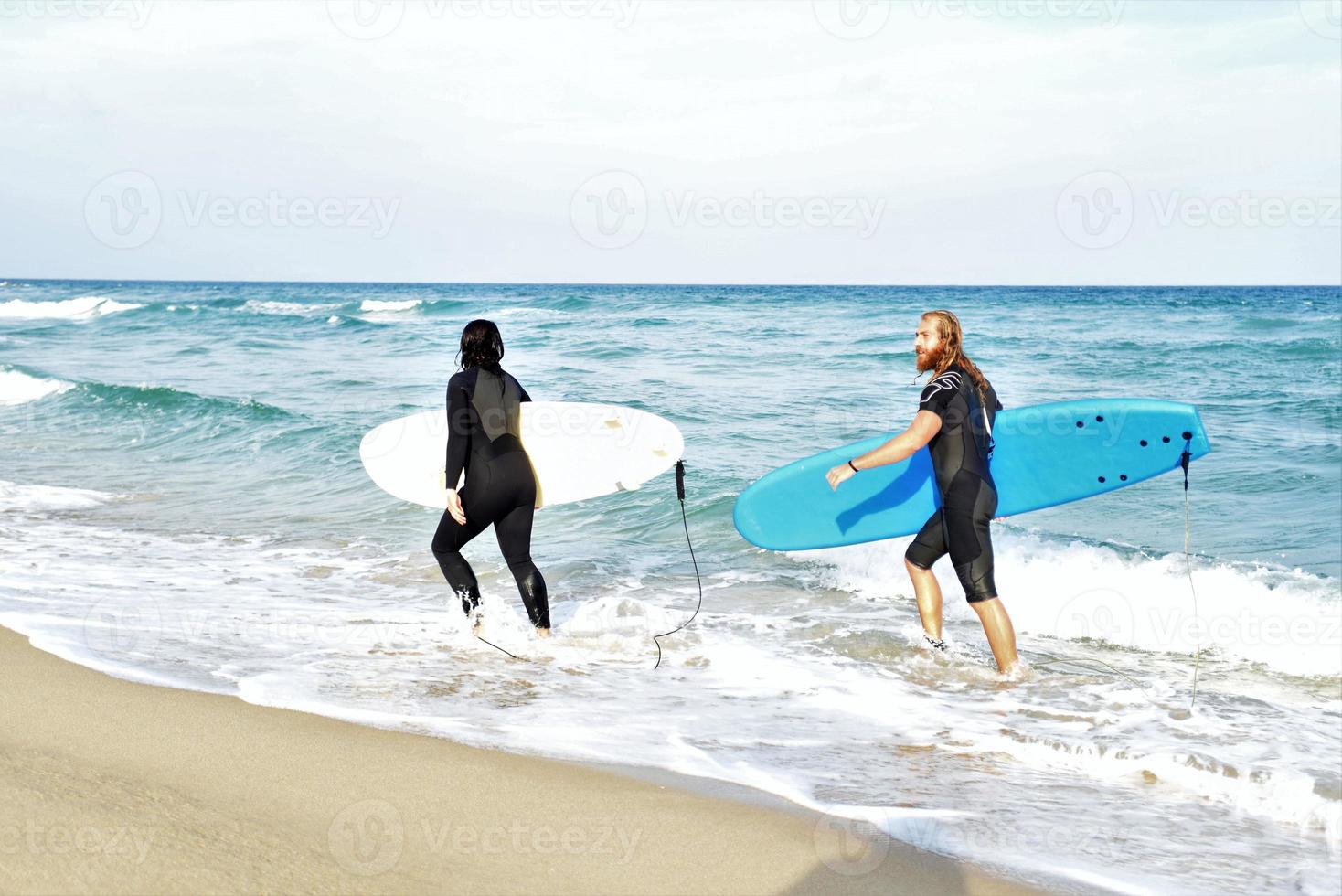 Surfers couple waiting for the high waves on beach - Sporty people with surf boards on the beach - Extreme sport and vacation concept photo