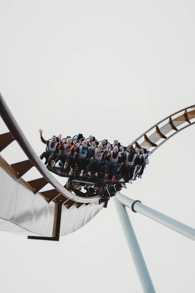 people having fun in amusement park. Young friends on thrilling roller coaster ride photo