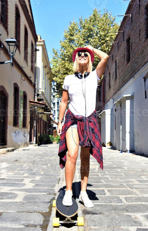Beautiful hipster girl with skate board wearing sunglasses in the city. photo